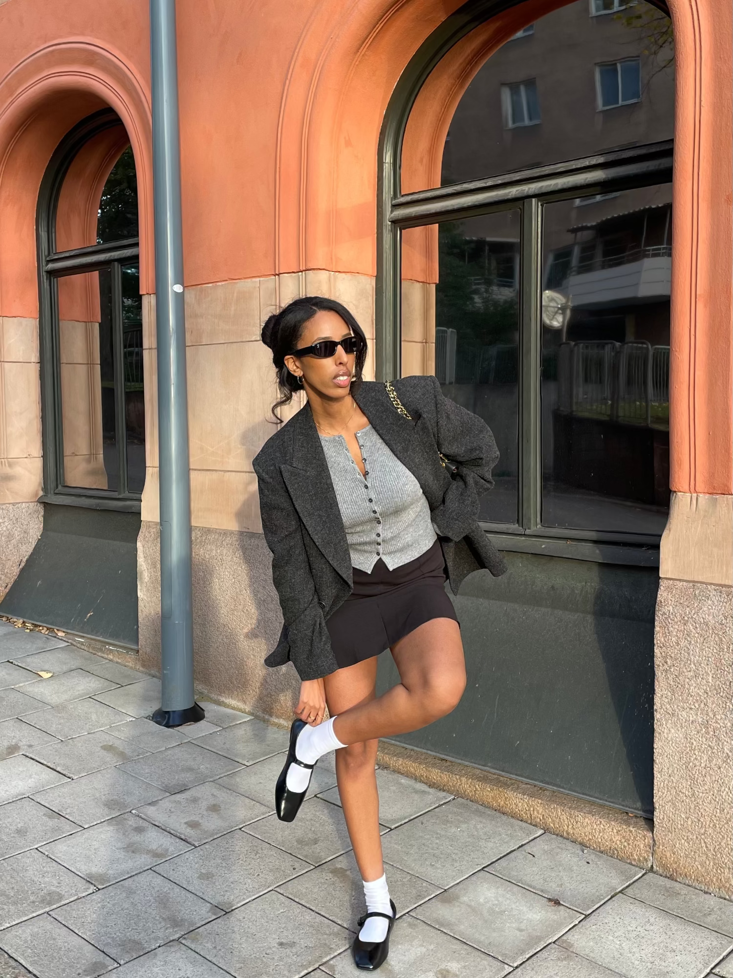 woman wearing a grey cardigan and outfit standing on one leg in front of a building