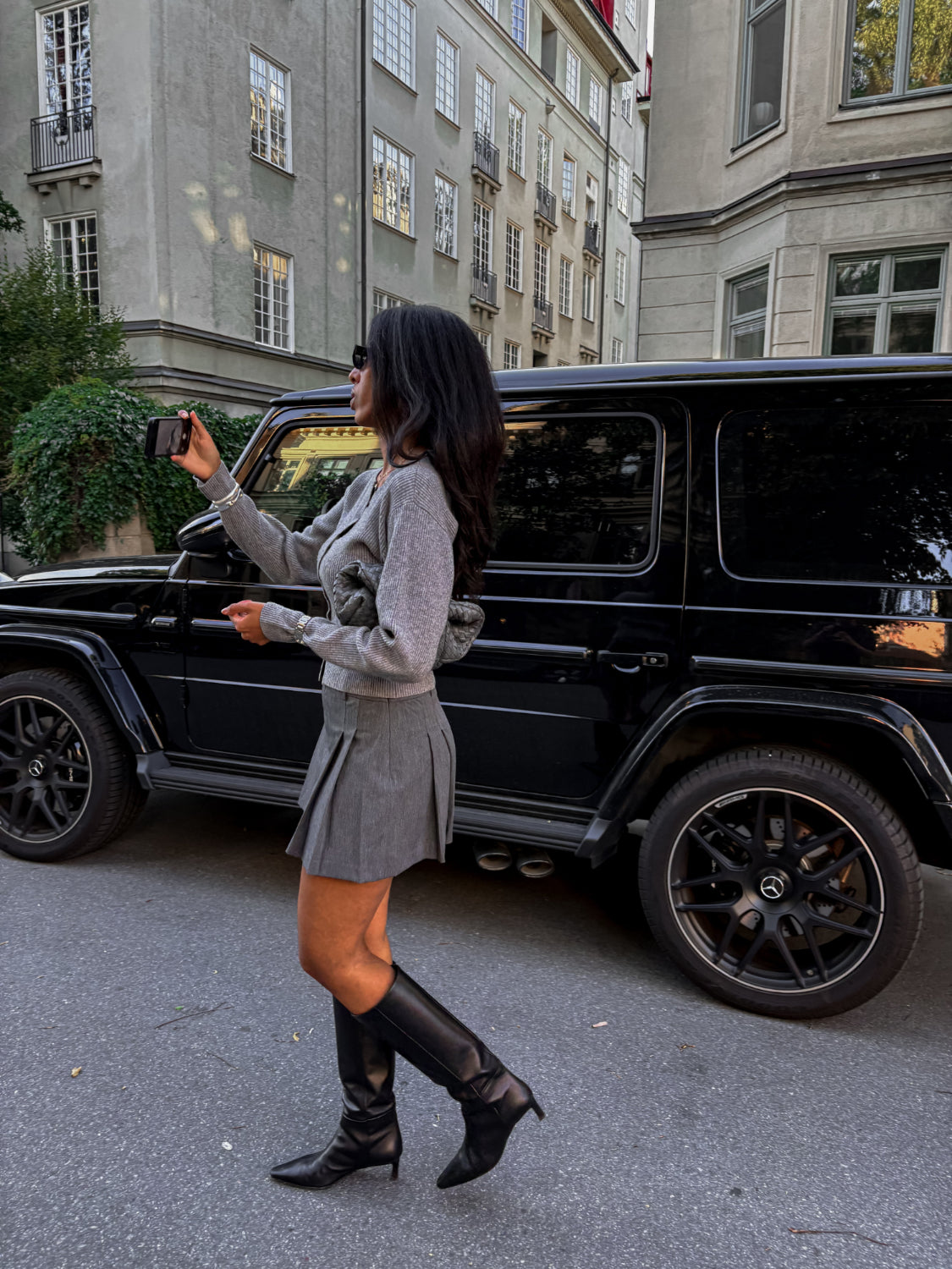 woman wearing a grey cardigan posing in front of a car